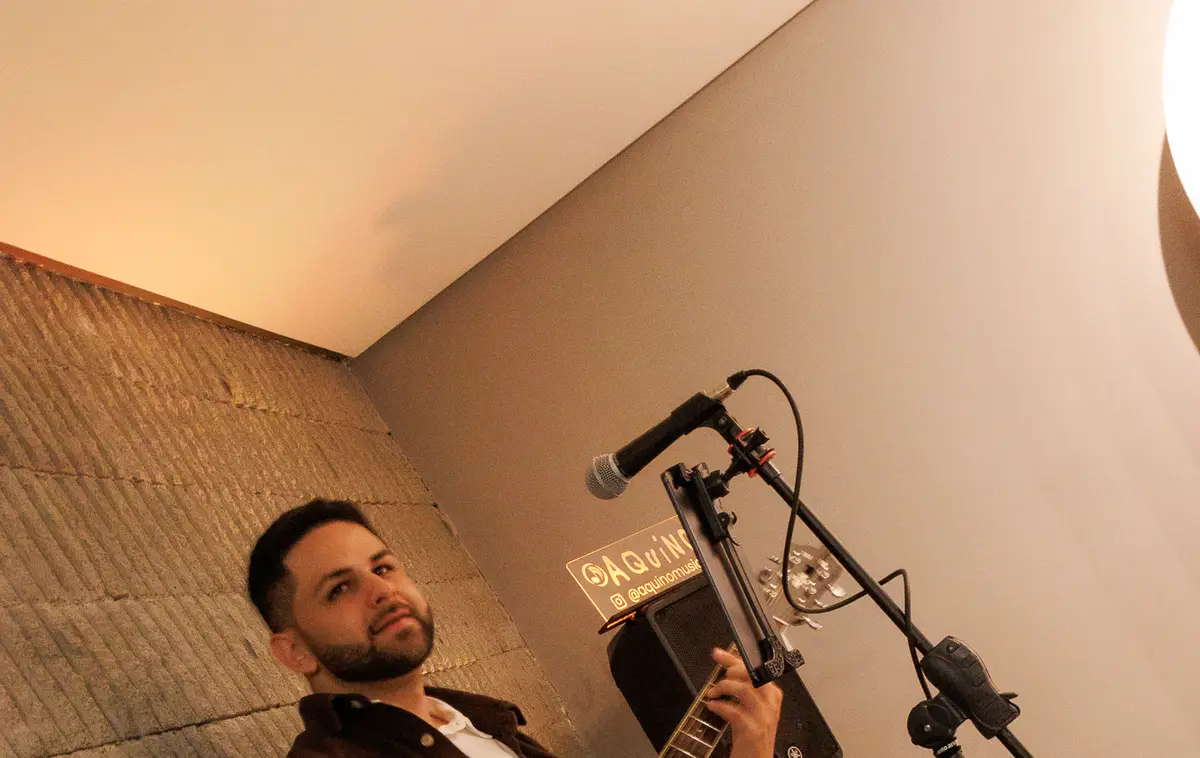 AQUINO, músico de voz e violão, em apresentação ao vivo.