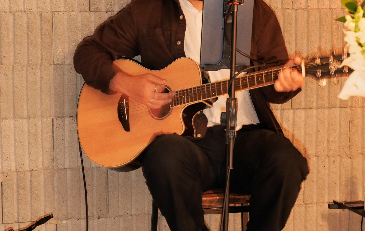 Detalhe das mãos de AQUINO tocando violão ao vivo.