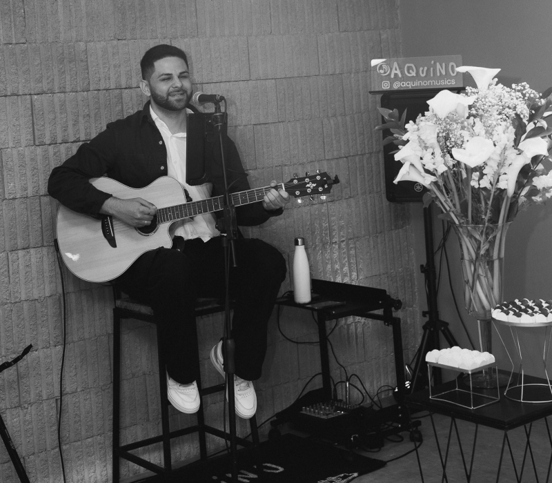 Foto profissional do músico Aquino com seu violão, demonstrando versatilidade de repertório para eventos.